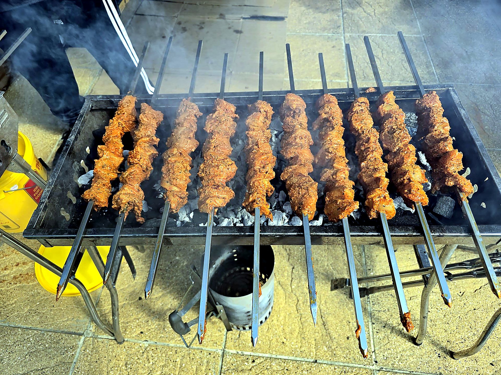 Chicken tikka skewers grilling over live charcoal in thick barbecue smoke